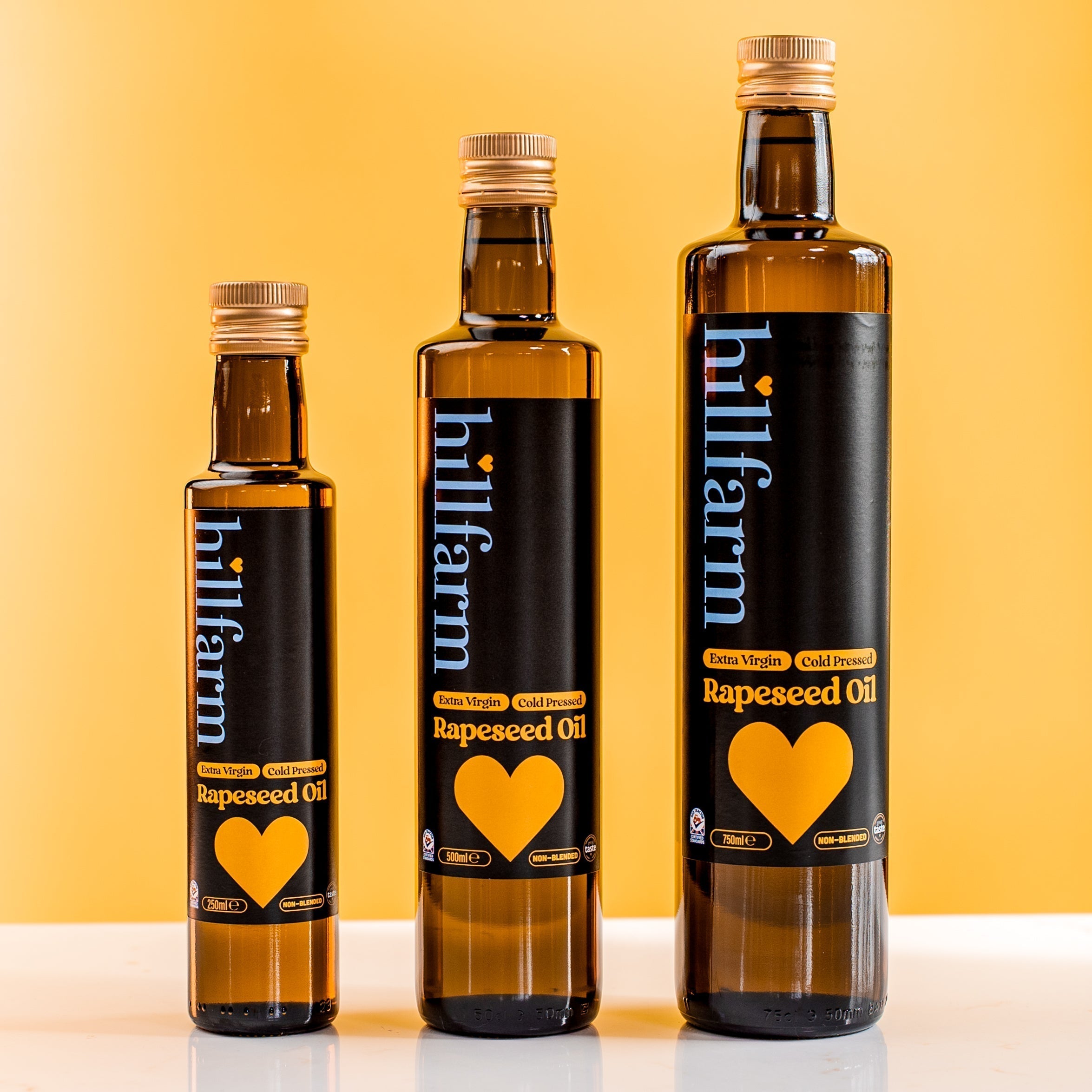 Hillfarm rapeseed oil bottles lined up in size order against a bright yellow backgoround